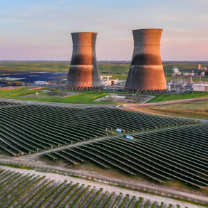 Aerial view of a power plant with cooling towers next to a large solar panel array at sunset