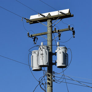 Power distribution transformers mounted on a utility pole against a clear blue sky